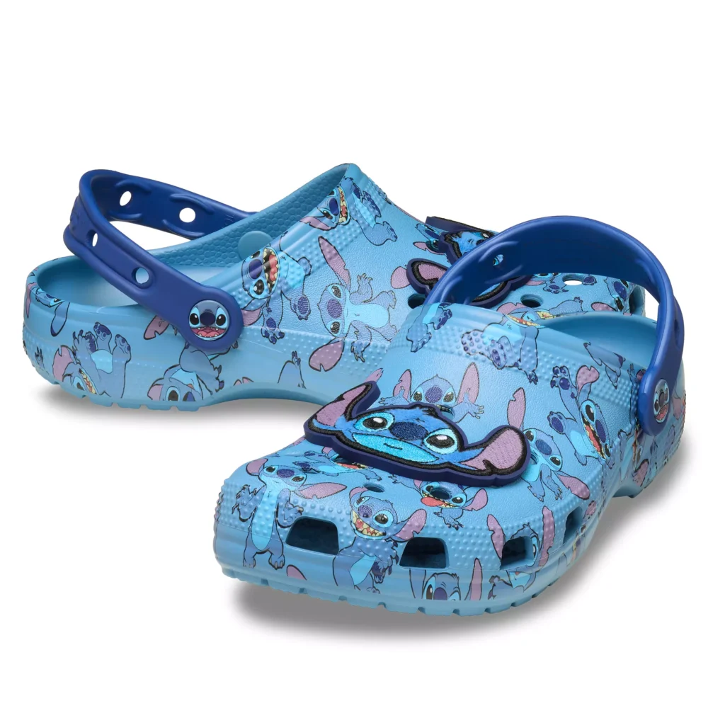 epasang Crocs Stitch warna biru langit dengan Jibbitz bordir dan mata Stitch berbinar di atas lantai studio putih